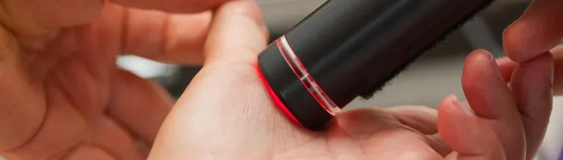 Um dispositivo preto com luz vermelha a tocar na pele da mão — Consultas