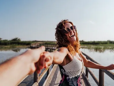Mulher sorridente a segurar a mão de alguém numa ponte de madeira — Saúde Sexual Feminina