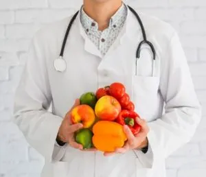 Médico com estetoscópio segura frutas e legumes coloridos