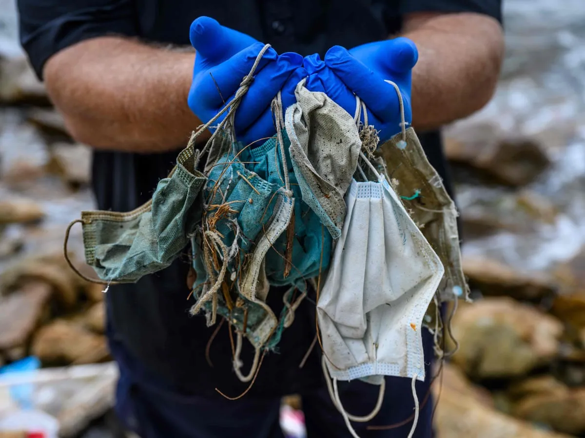 Mãos com luvas azuis seguram máscaras sujas e danificadas