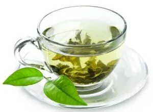 Chávena de chá verde com folhas e duas folhas frescas ao lado — 10 alimentos que melhoram a saúde e a potência
