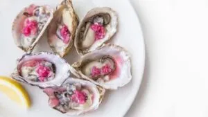Ostras cozidas com molho rosa e limão num prato branco — 10 alimentos que melhoram a saúde e a potência