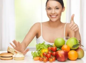 Mulher a sorrir com frutas e legumes na mesa — Como proteger o nosso DNA