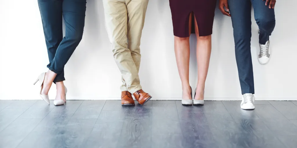 Quatro pessoas de pé com sapatos diferentes num chão cinzento e parede branca — Gestos que falam – os sinais escondidos